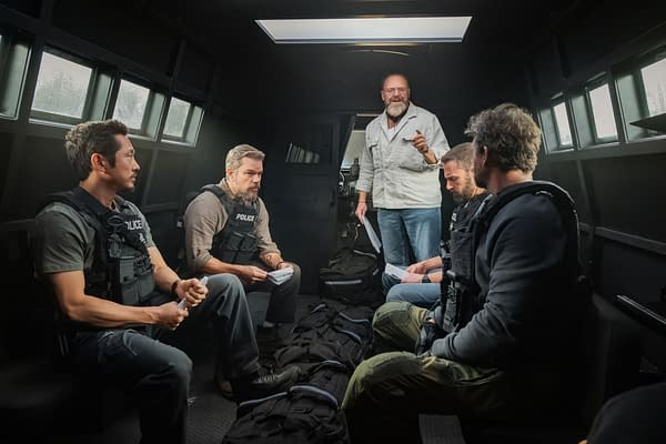 On the set of 'The Rip,' a group of actors, including Steven Yeun, Matt Damon, Ben Affleck, and Kyle Chandler, sit attentively while director Joe Carnahan gives instructions inside a police vehicle. Each actor wears a tactical vest, emphasizing the film's action theme.