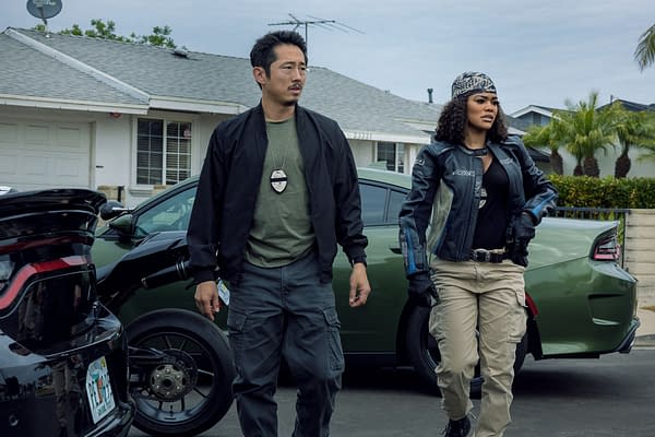 Two detectives, Steven Yeun as Detective Mike Ro and Teyana Taylor as Detective Numa Baptiste, walk together in an urban setting. The background features homes and cars, indicating an investigative scene from the Netflix series 'The Rip'.
