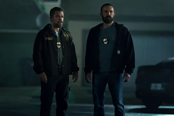 A dramatic scene from the Netflix series 'The Rip,' featuring two male officers, one in a brown police jacket and the other in a black hoodie, both wearing police badges. They appear serious and are positioned outdoors at night.
