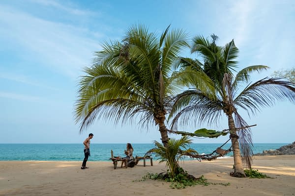 Dylan O'Brien as Bradley Preston and Rachel McAdams as Linda Liddle are shown on a beach, with palm trees and the ocean in the background, in a scene from 20th Century Studios' 'SEND HELP.'