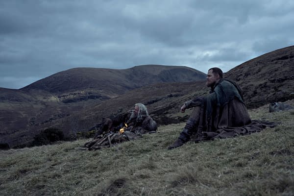 A scene depicting two men seated by a small fire on a grassy hillside, surrounded by rolling hills under a cloudy sky, conveying a sense of solitude and reflection. This image relates to 'The Death of Robin Hood.'