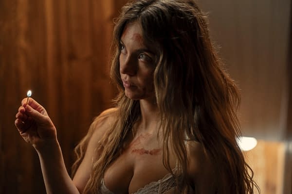 A woman with long, wavy hair holds a lit matchstick, her face showing signs of distress with markings on her skin, suggesting a tense atmosphere. This scene features Sydney Sweeney as Millie Calloway from 'The Housemaid.'