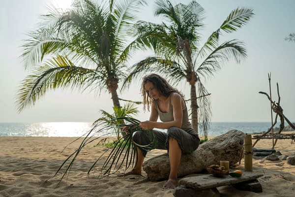 Rachel McAdams as Linda Liddle on a beach, surrounded by palm trees, focused on weaving leaves. The serene ocean can be seen in the background, reflecting soft light.
