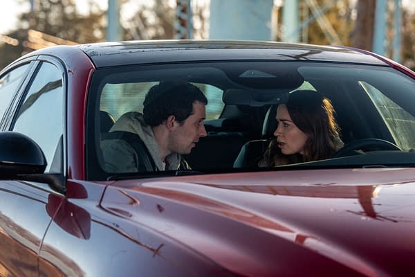 A scene from the film 'DISCLOSURE DAY' features two characters, portrayed by Josh O'Connor and Emily Blunt, engaged in an intense conversation inside a red car. The exterior shows a blurred background with soft lighting, suggesting a tense moment.