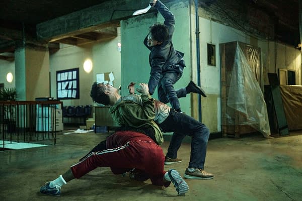 A dramatic fight scene unfolds in a dimly lit interior space, featuring two men struggling on the ground while a third man leaps above them, wielding a weapon. The tense atmosphere and dynamic poses highlight the action and intensity of the moment.