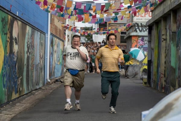 Two men, one wearing a 'New York City' t-shirt and the other in a patterned yellow shirt, run down a lively alley decorated with colorful banners and street art, conveying a sense of excitement and urgency.