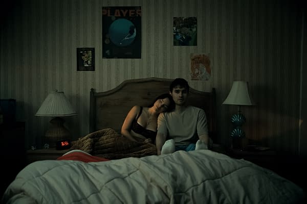 A dramatic scene from the film 'Obsession' featuring Inde Navarrette as Nikki leaning on Michael Johnston as Bear in a dimly lit bedroom, with posters on the walls and a clock showing 16:55.