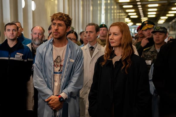 Ryan Gosling as Ryland Grace and Sandra Hüller as Eva Stratt stand among a group of scientists and military personnel, showing a moment of serious discussion on the set of the film Project Hail Mary.
