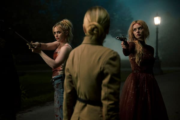 A dramatic scene from 'Ready Or Not 2: Here I Come' features three women in a tense standoff under dim lighting, with one holding a sword and another aiming a gun. The eerie atmosphere is accentuated by fog and a distant street lamp.
