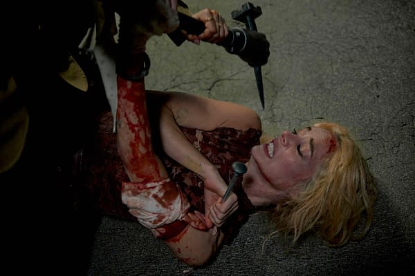 A scene from 'READY OR NOT 2: HERE I COME' featuring a bloodied woman in a torn dress, lying on the ground with a distressed expression. A figure looms over her, holding a weapon, suggesting a tense and dramatic moment.
