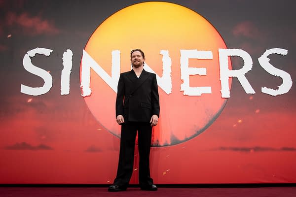 Jack O'Connell stands in front of a large backdrop featuring the title 'Sinners' against a vibrant red background and a stylized sun. This image captures the European premiere of the film, highlighting the excitement of the event.