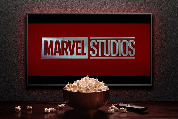 A close-up illustration featuring a television screen displaying the MARVEL STUDIOS logo, set against a bold red background. A bowl of popcorn sits in front, alongside a remote control, creating a cozy movie-watching atmosphere.