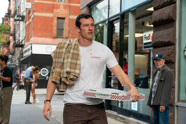 Callum Turner as Owen walks down a city sidewalk carrying pizza boxes and a plaid shirt over his shoulder in One Night Only.