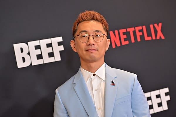 A man with light brown hair and glasses, wearing a light blue suit, stands in front of a black backdrop featuring the text 'BEEF' and 'NETFLIX.' He has a small pin on his suit.