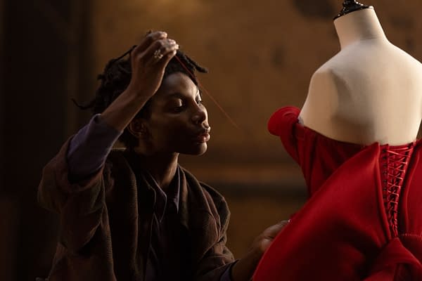 A fashion designer focuses intently while sewing a vibrant red dress on a mannequin, showcasing creativity and craftsmanship.