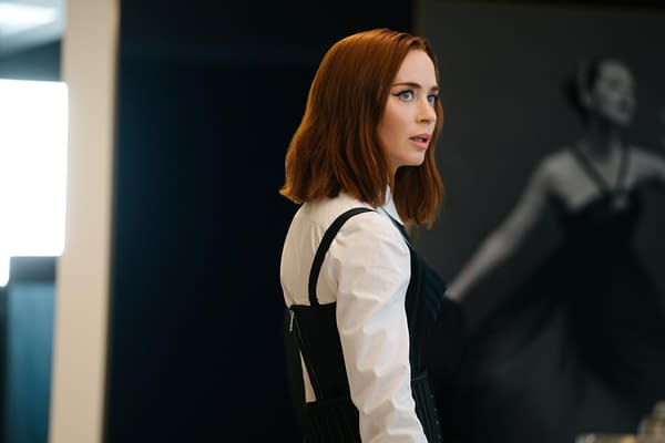 A red-haired woman in a white shirt and black corset-style dress looks off to the side in a fashion boutique, suggesting a scene from The Devil Wears Prada 2.