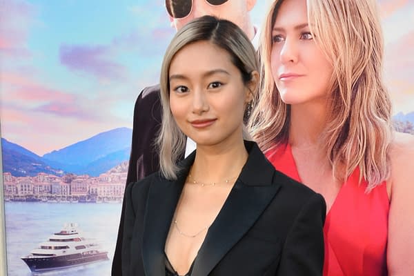 A woman with light hair styled in a bob, wearing a black suit jacket, stands smiling in front of a colorful background featuring mountains and a luxury yacht. This image appears to be related to a promotional event.