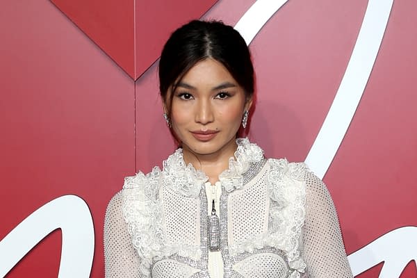 A woman poses confidently in a stylish outfit adorned with ruffles and sparkly accents, set against a vibrant red background. This image relates to the casting announcement for the upcoming live-action Gundam film.