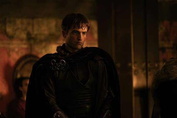 Robert Pattinson stands in dark armor and a cape in a moody scene from The Odyssey.