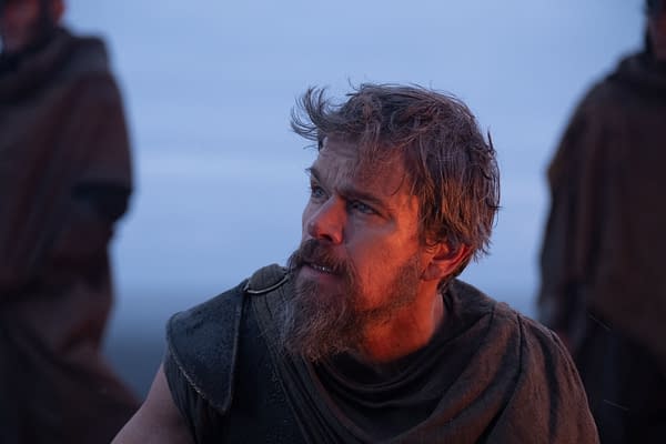 Matt Damon as Odysseus in The Odyssey, looking upward in rugged ancient costume with warm firelight on his face.