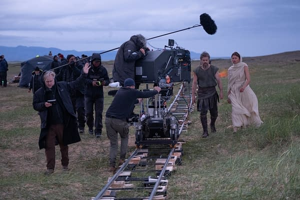 On-set filming of The Odyssey with Christopher Nolan, Matt Damon as Odysseus, and Zendaya as Athena beside an IMAX camera on a track in a windy field.