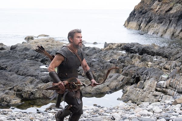 Matt Damon as Odysseus stands on a rocky shoreline holding a bow and arrows in The Odyssey.