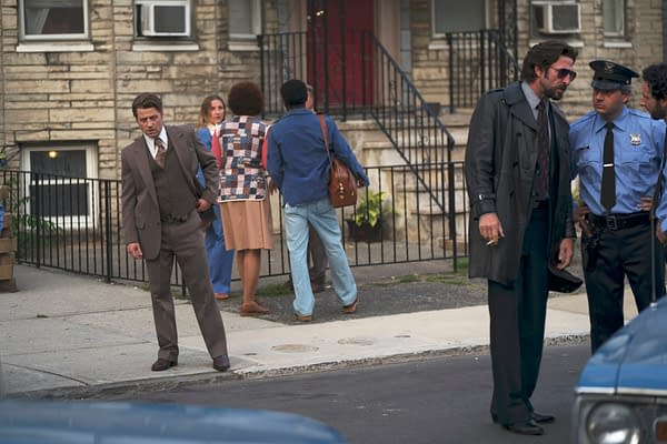 Film still from Motor City showing a tense street scene with a suited man, a trench-coated man, and police officers outside an apartment building.