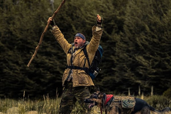 Brad Pitt as James Belmont stands outdoors with arms raised and holding a long branch, beside a saddled German shepherd named Odin in Heart of the Beast.
