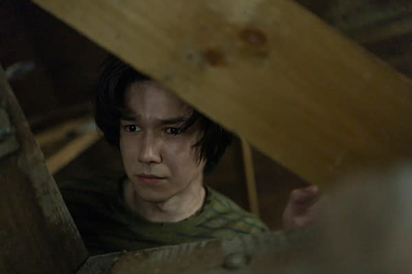 Gabriel Barbosa as Graham peers through a narrow opening in a dim, cramped space in The Last House.