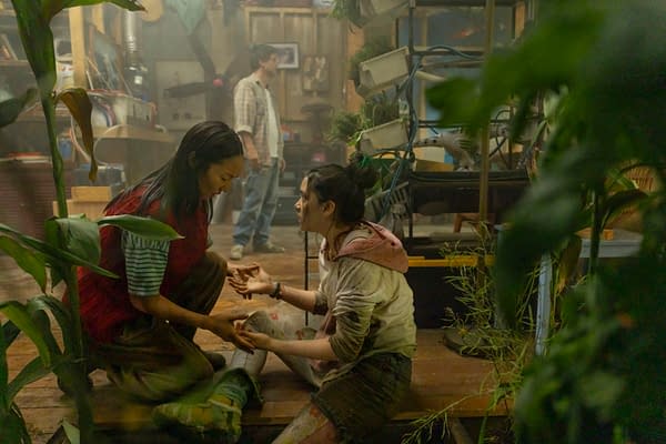 Greta Lee and Emma Ho kneel face to face in a cluttered greenhouse-like room while Wagner Moura stands in the background in The Last House.