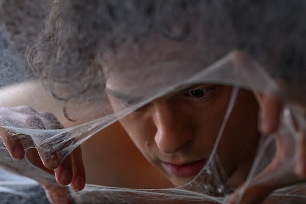 Close-up of a young Spider-Man star peering through strands of webbing with a focused expression.