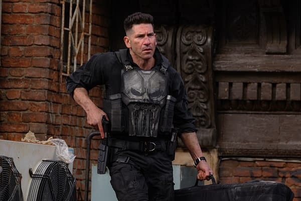 Frank Castle, in black tactical gear and body armor, carries a duffel bag in an urban alley set from Spider-Man: Brand New Day.