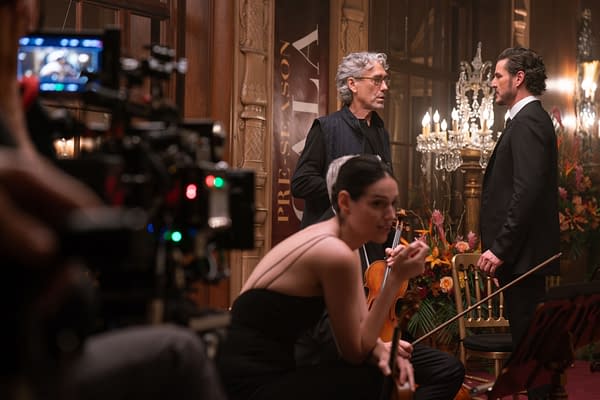 Director Tony Gilroy talks with Pedro Pascal on the set of BEHEMOTH!, while Eva Victor sits in the foreground holding a violin.