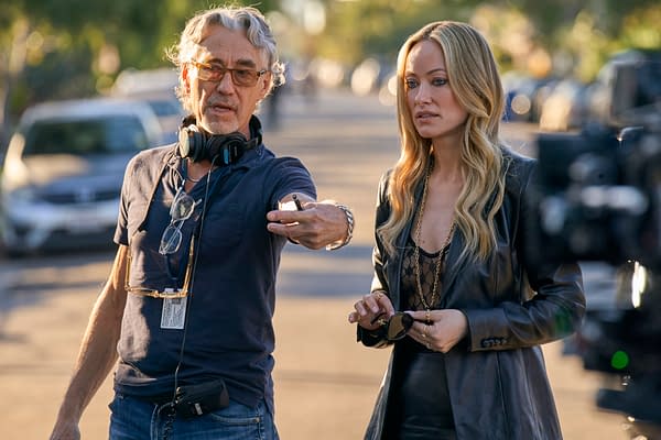 Director Tony Gilroy gestures beside Olivia Wilde on the set of BEHEMOTH!, with film equipment and a sunlit street in the background.