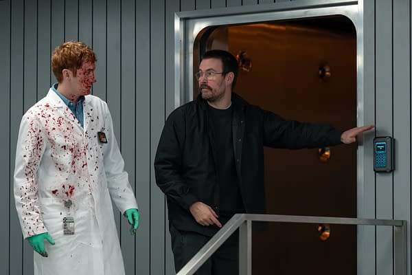 Two men stand in a sleek elevator doorway, one in a blood-splattered lab coat and green gloves, the other pointing toward a keypad in a tense Resident Evil scene.