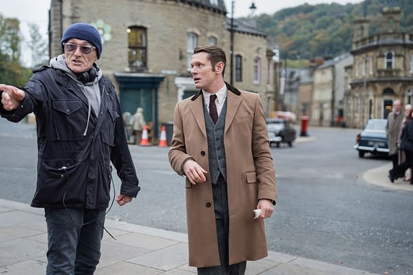Director Danny Boyle gestures on the set of INK beside Jack O'Connell in a tan overcoat on a street set.