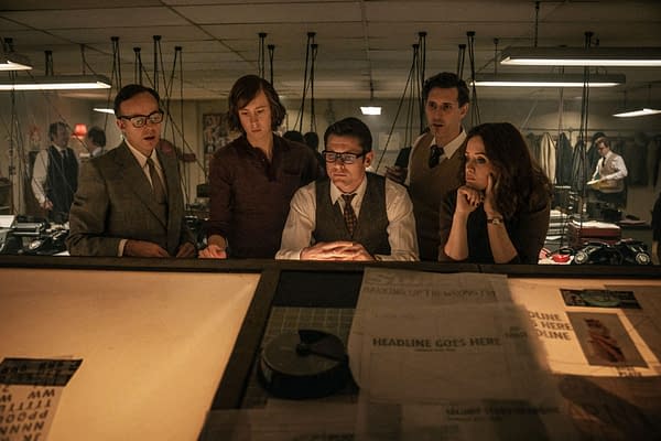 Jack O'Connell and Claire Foy stand with three colleagues in a dimly lit newsroom, looking down at a desk covered with paper layouts and headlines for Ink.