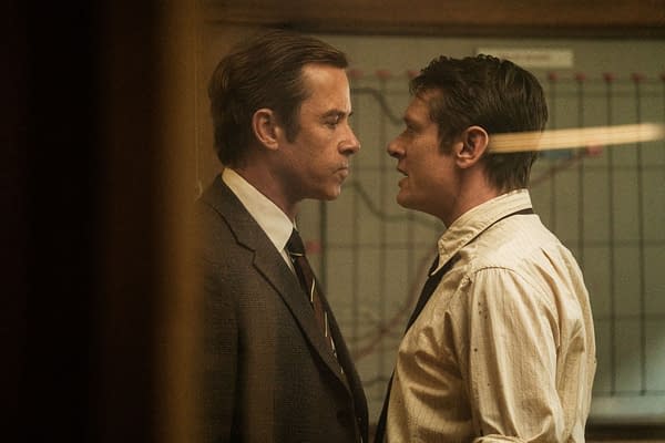 Guy Pearce and Jack O'Connell stand face to face in a tense scene from Ink, dressed in suits and a white shirt in a dim office setting.