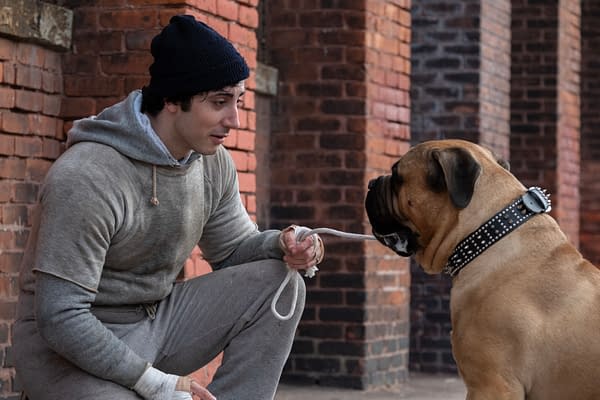 Anthony Ippolito, as Sylvester Stallone in I PLAY ROCKY, crouches beside a large dog on a leash in front of a brick wall.