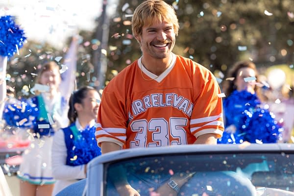 David Corenswet smiles in an orange Irrelevant No. 335 jersey as confetti falls around him at a celebratory parade.