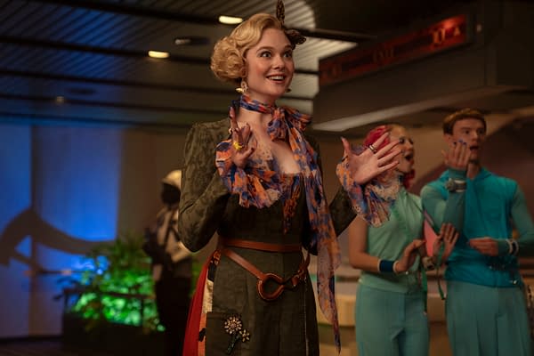 Elle Fanning as Effie Trinket smiles in a colorful retro outfit with styled blonde hair in The Hunger Games: Sunrise on the Reaping.