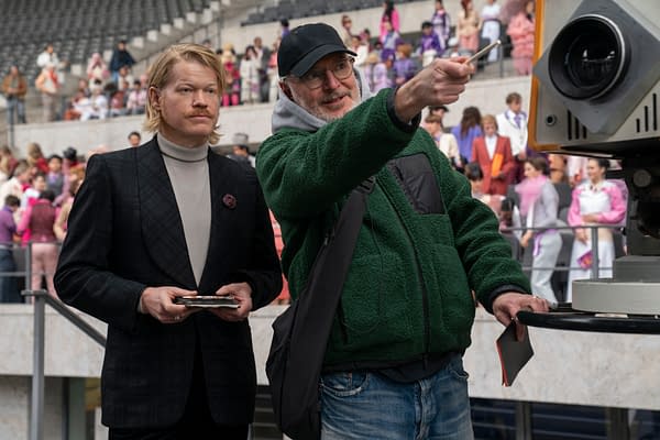 Jesse Plemons stands beside director Francis Lawrence on the set of The Hunger Games: Sunrise on the Reaping, with Lawrence pointing toward a camera in a stadium filled with extras.