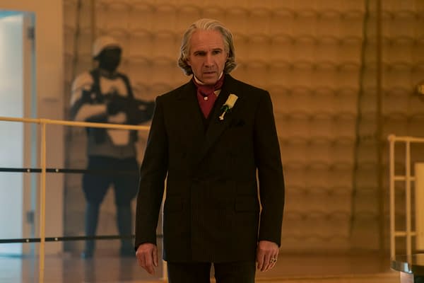 Ralph Fiennes as President Snow stands in a dark suit with a white boutonniere in The Hunger Games: Sunrise on the Reaping.