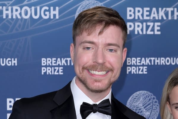 A man wearing a tuxedo with a bow tie smiles at the camera, standing in front of a blue background featuring the text 'Breakthrough Prize'. He has light brown hair and a trimmed beard.