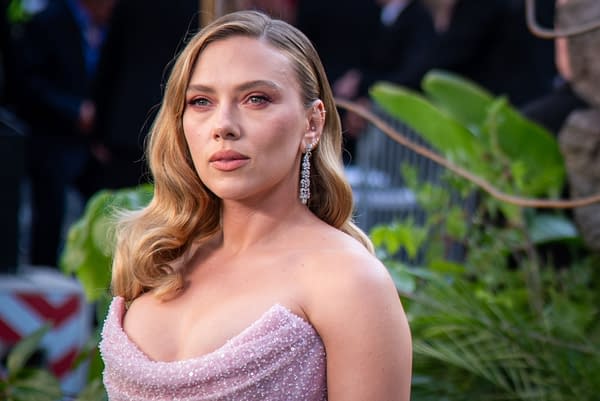 Scarlett Johansson poses on the red carpet at a London screening, wearing a sparkling pink gown and statement earrings, surrounded by lush green foliage.