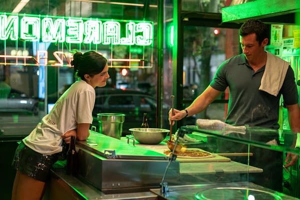 Two people chat at a neon-lit pizza counter while one stretches dough and adds sauce. Green Gremona sign reflections glow in the window behind them.