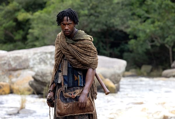 Tosin Cole as Tzain stands in a rugged costume beside a river in Children of Blood and Bone.