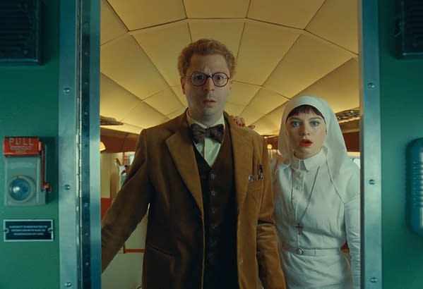 In a scene from 'THE PHOENICIAN SCHEME,' Michael Cera as Bjorn and Mia Threapleton as Liesl stand at the entrance of a colorful, retro-futuristic set, displaying expressions of surprise and curiosity.