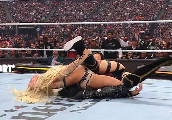 A dramatic moment from a wrestling match at WrestleMania, showcasing two female wrestlers in a competitive hold, with a large crowd visible in the background.