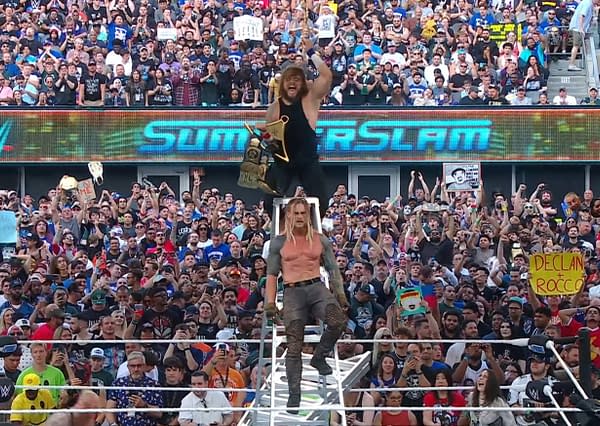 A victorious wrestler stands atop a stack of chairs, holding a championship belt and celebrating in front of a cheering crowd at a wrestling event. The large electronic display shows 'SUMMERSLAM.'